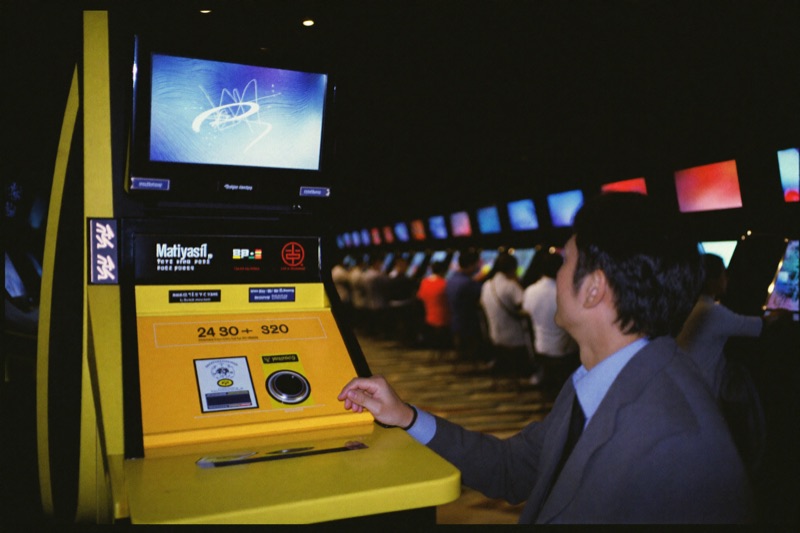 The floor from a supervisor's position, a man in a suit looking down a long row of slot cabinets with players at most of them