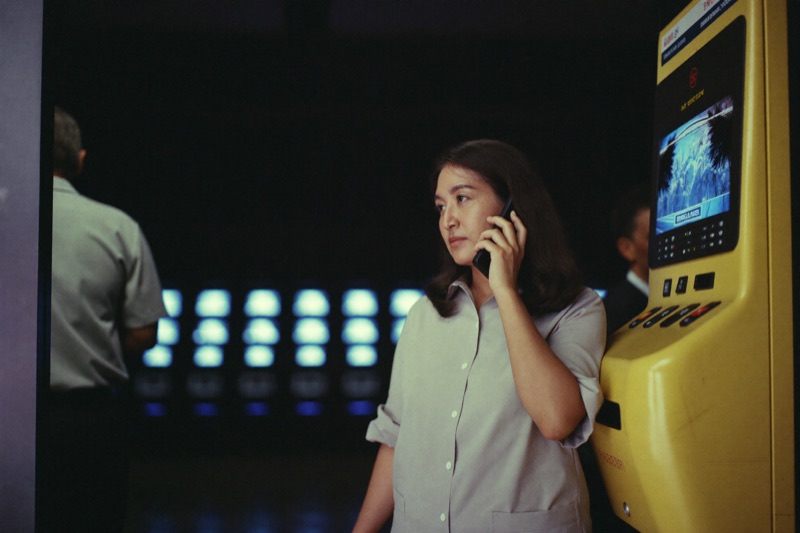 A woman standing at the entrance to a slot hall tapping a password into her phone, the lit cabinets of the floor out of focus behind her
