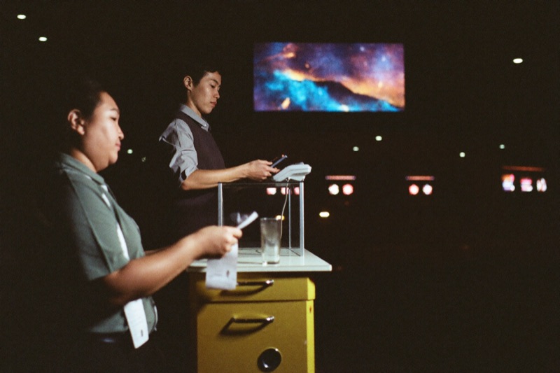 A player at the cash desk taking a payout from a cashier behind the counter glass, a receipt on the ledge and a lit slot hall behind him