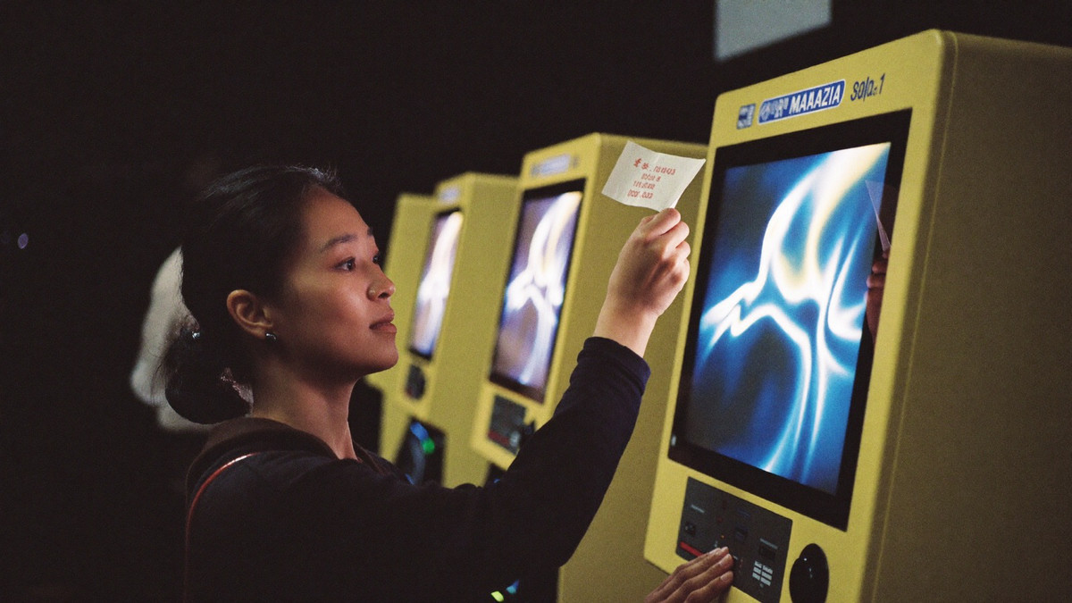 A woman at a slot cabinet holding a small paper voucher up beside the screen with her other hand on the spin button