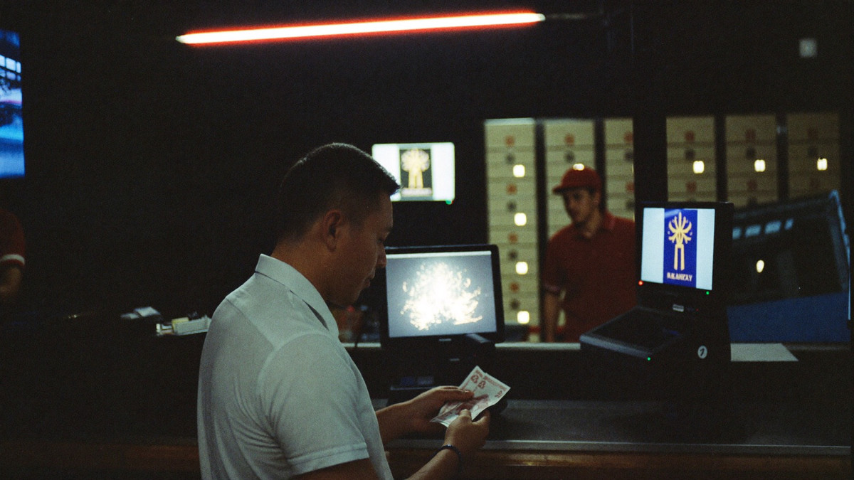 A player at the cash desk watching the cashier count notes into his hand, slot cabinets lit behind him